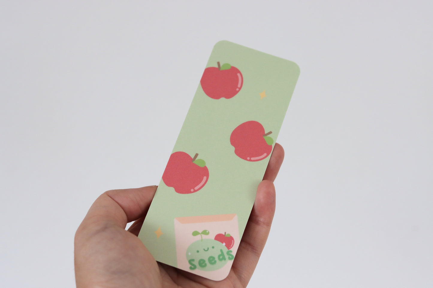 A hand holding a green bookmark with an apple pattern
