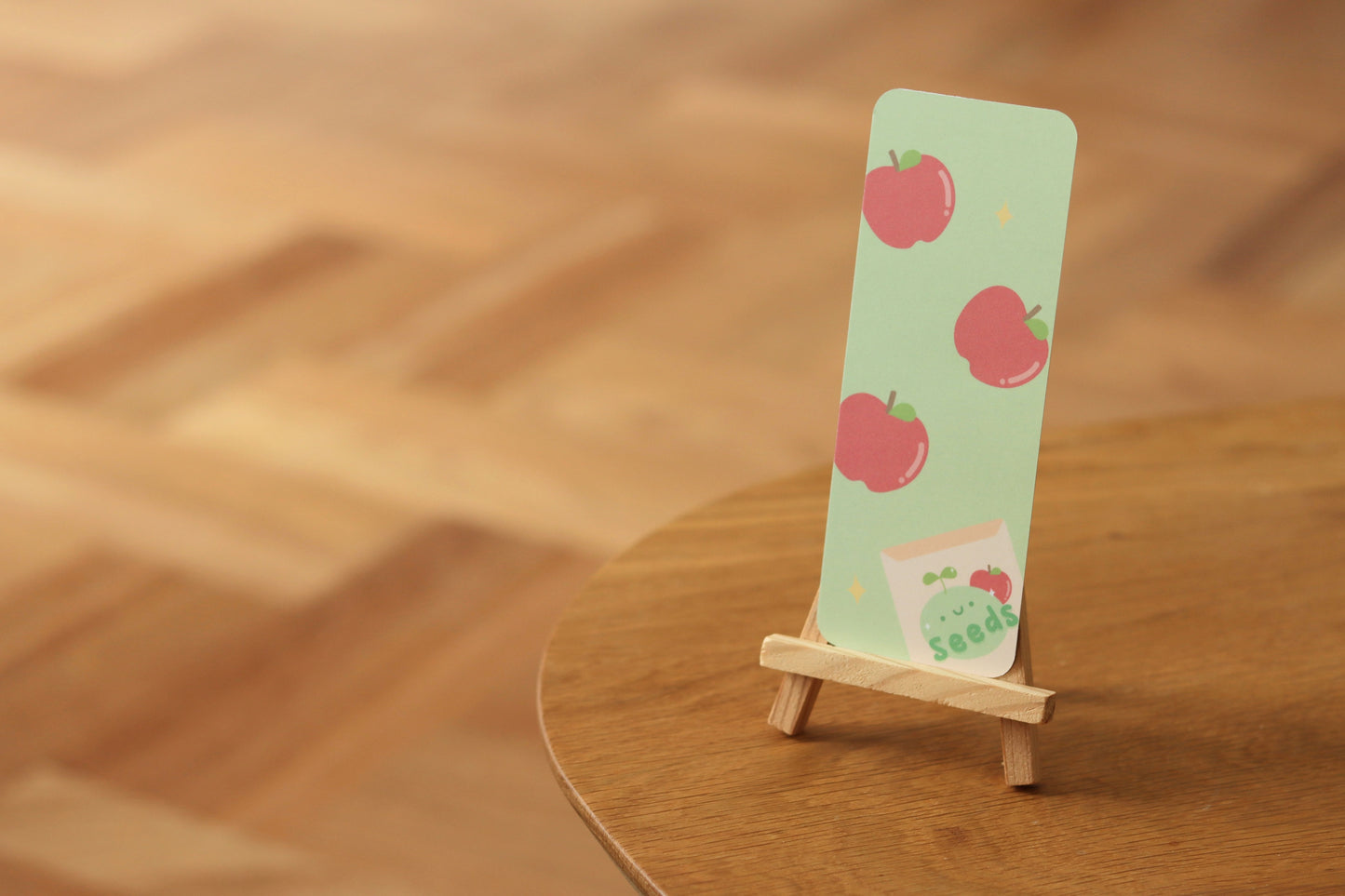A green bookmark with apples and an apple seed package on a table