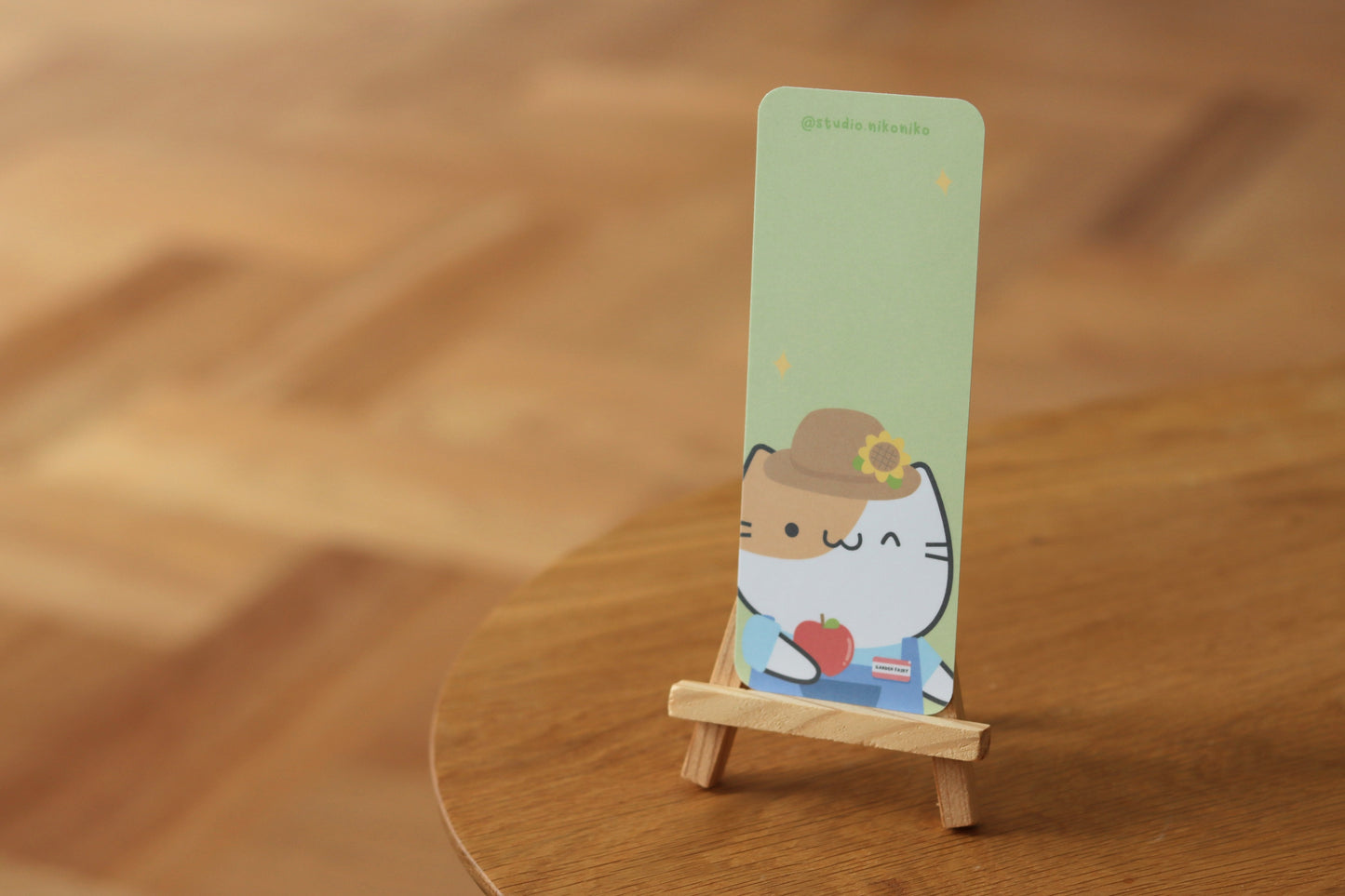 A green bookmark with a cat in gardening clotheson a table