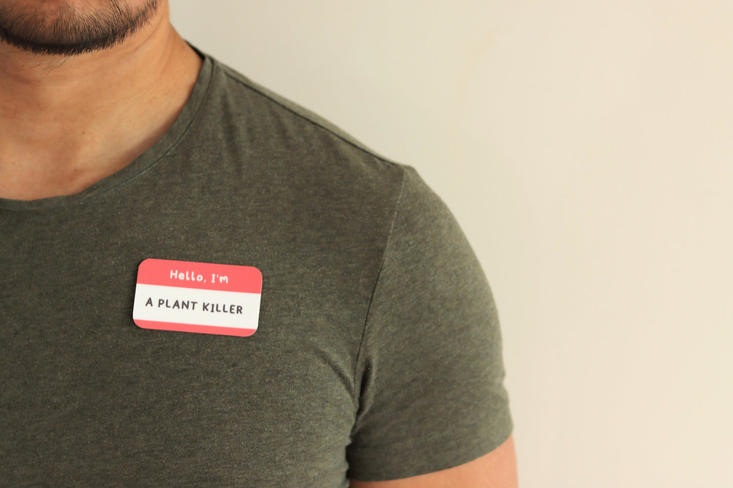 A man with a green t-shirt with a nametag sticker with the text: Hello, I'm a plant killer