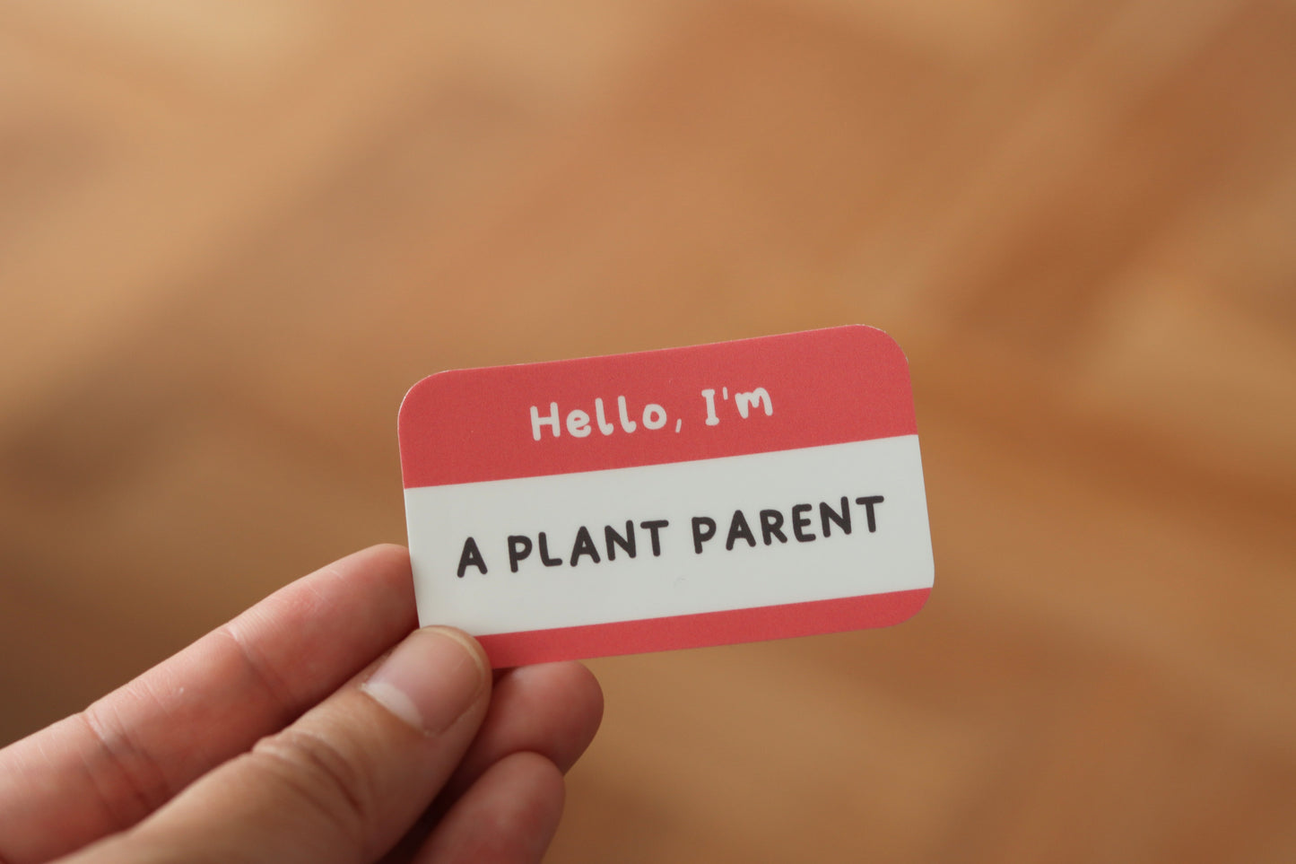 A hand holding a nametag sticker with the text: Hello, I'm a plant parent