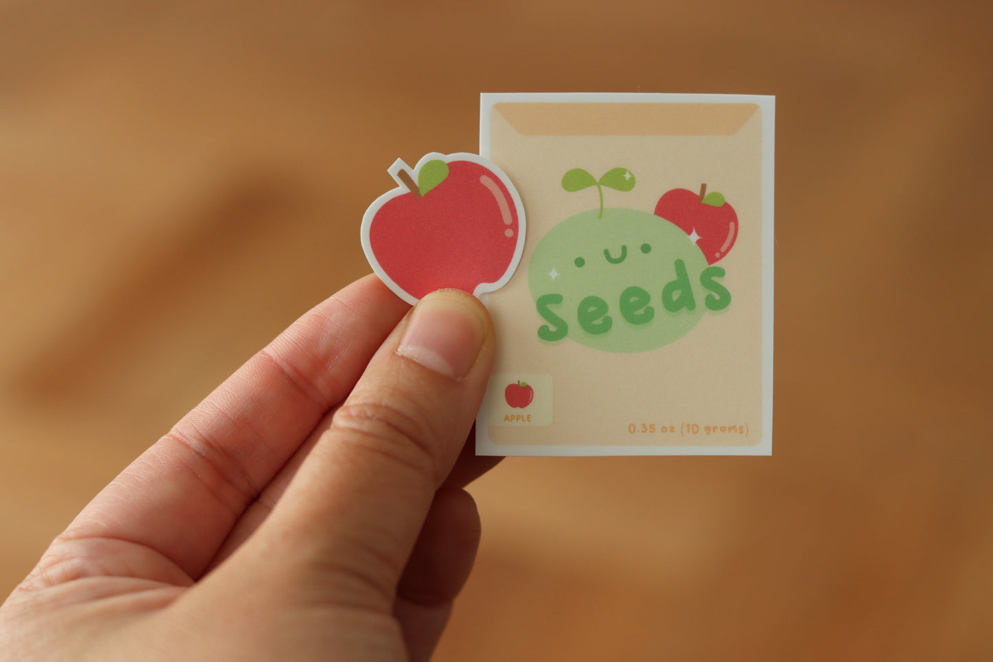 A hand holding an apple sticker and an apple seeds packaging sticker