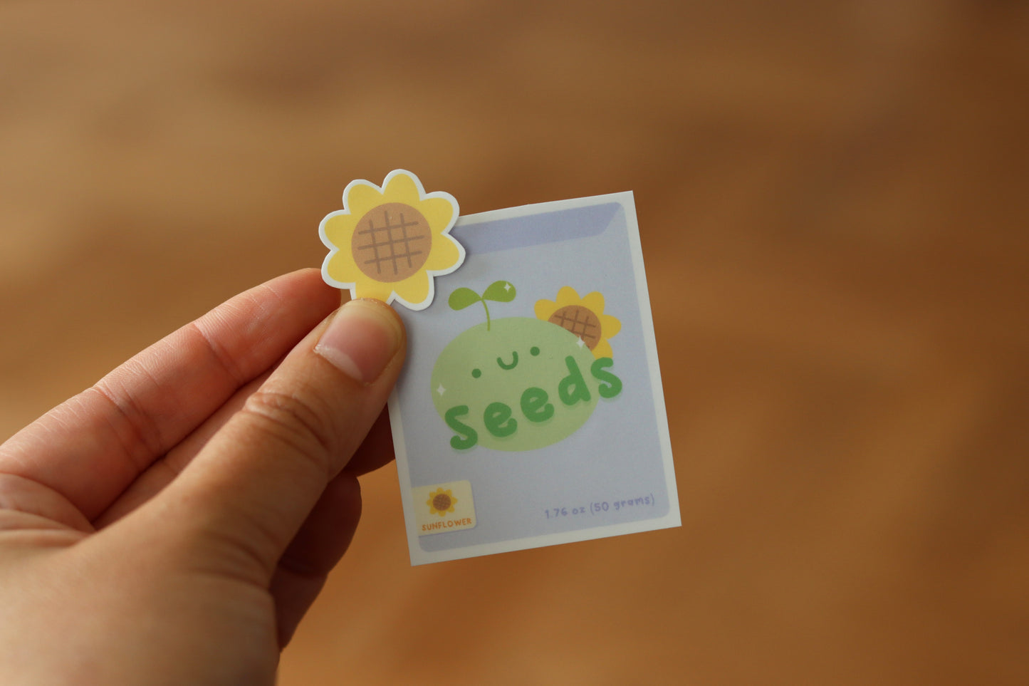 A hand holding a sunflower sticker and an sunflower seeds packaging sticker