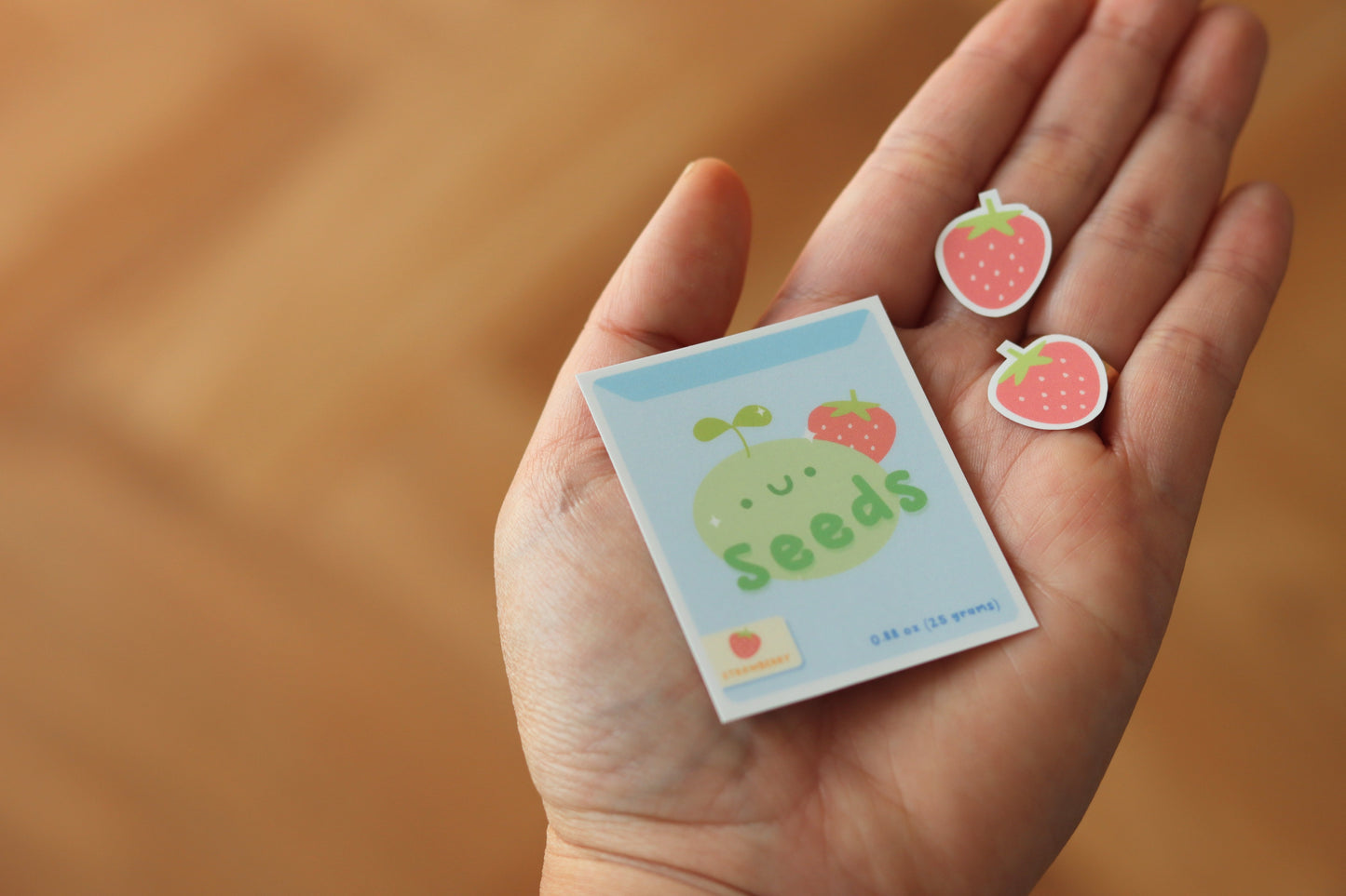 A hand holding two strawberry stickers and a strawberry seeds packaging sticker