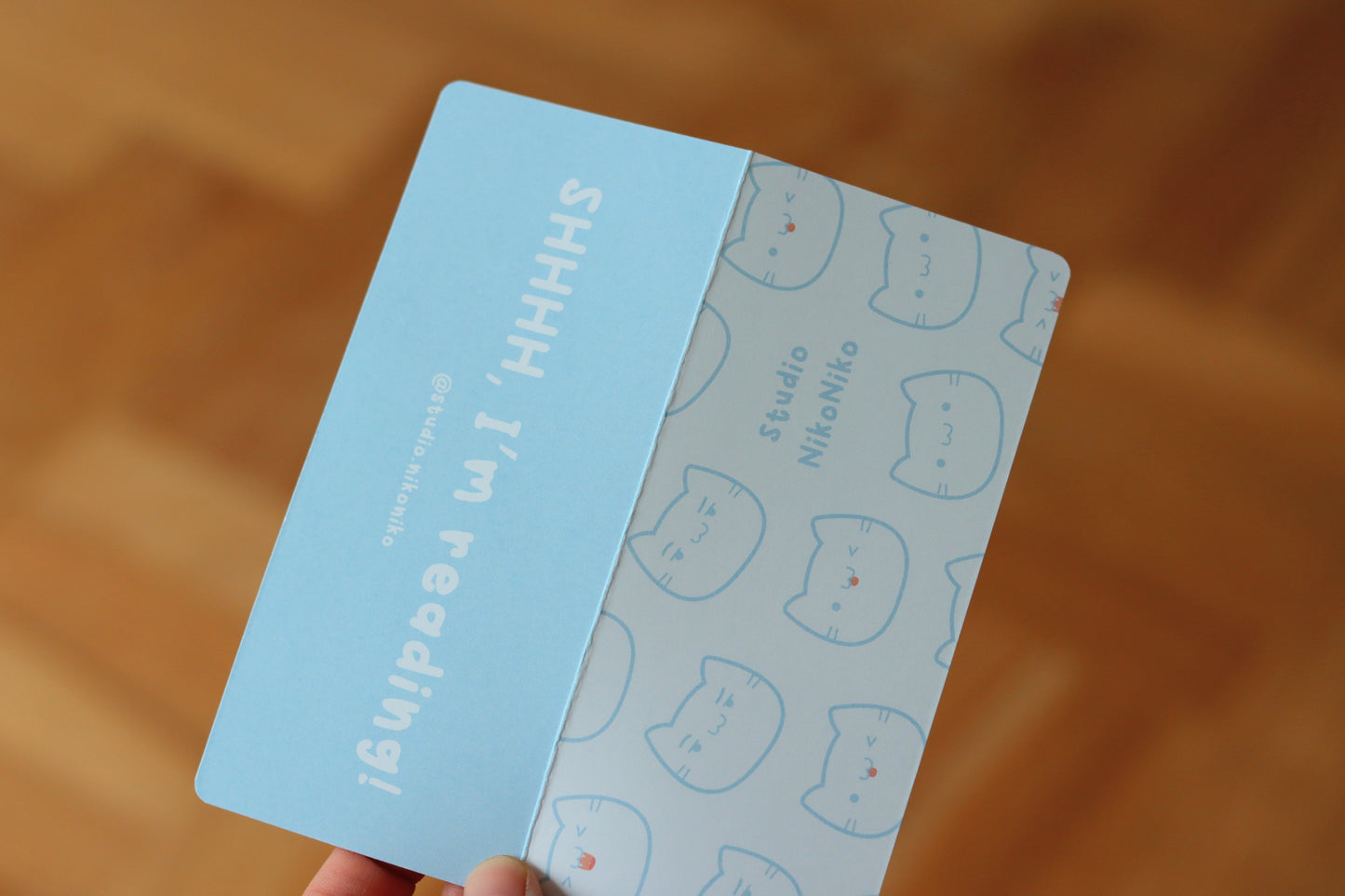 The packaging for bookmarks with a blue side that says: SHHH, I am reading! and on the other side a pattern of cat faces on a white background