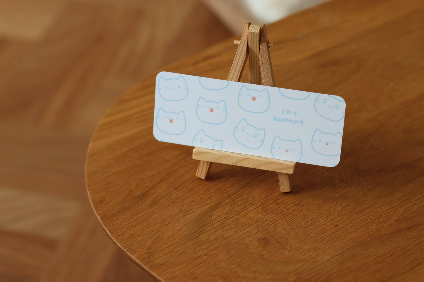 A white bookmark with a cat face pattern and the text: I'm a bookmark standing on a wooden table
