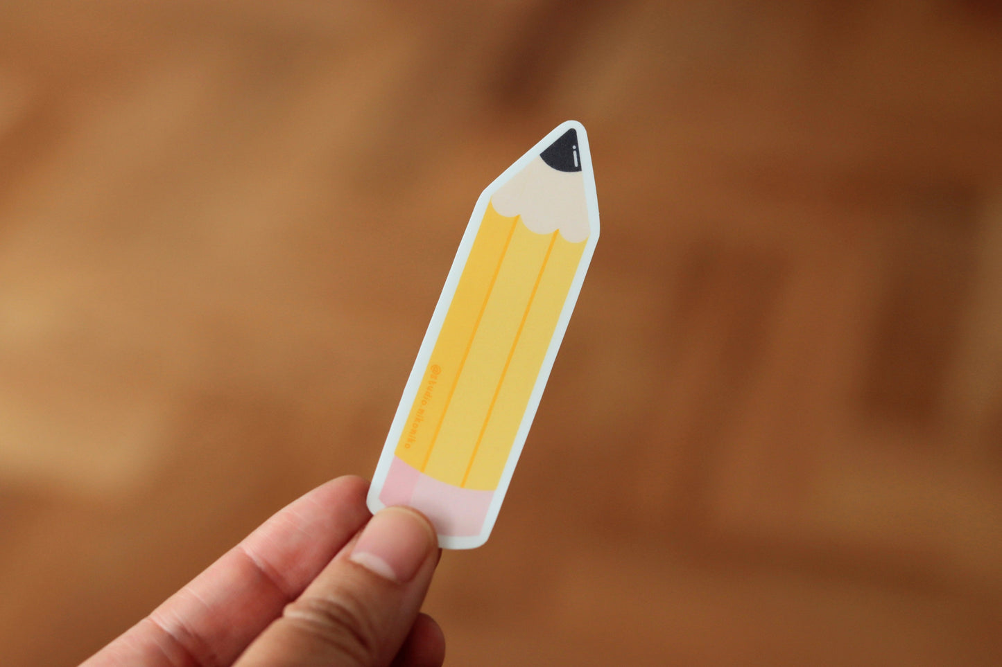 A hand holding a sticker design of a yellow pencil and pink eraser
