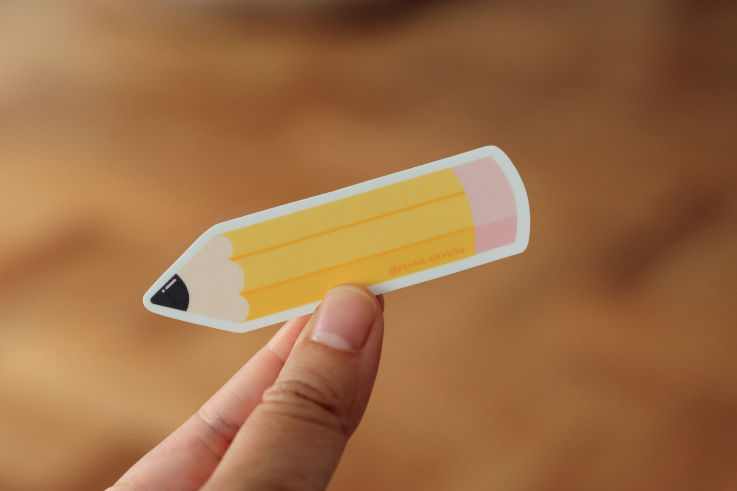 A hand holding a sticker design of a yellow pencil and pink eraser