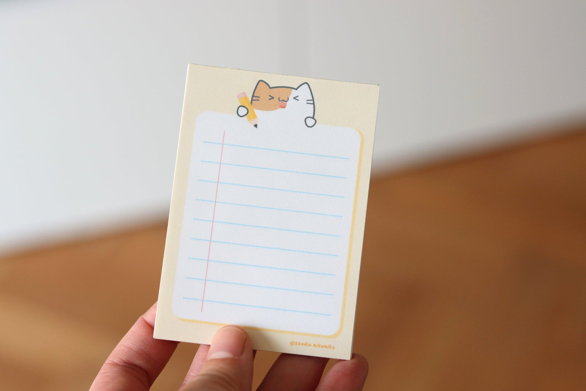 A hand holding a yellow notepad with a cat and a yellow pencil