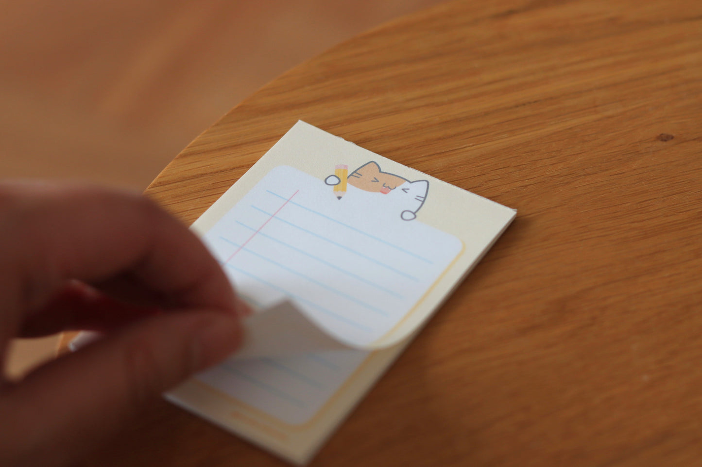 A hand tearing off a sheet of a yellow notepad with a cat and a yellow pencil