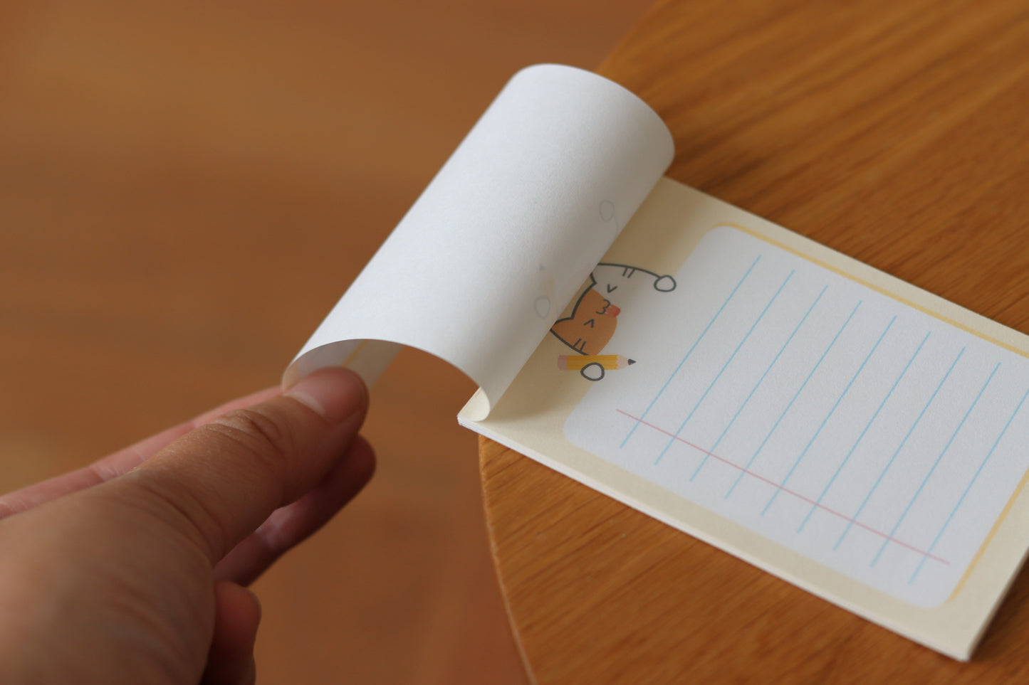 A hand holding a page of a yellow notepad with a cat and a yellow pencil