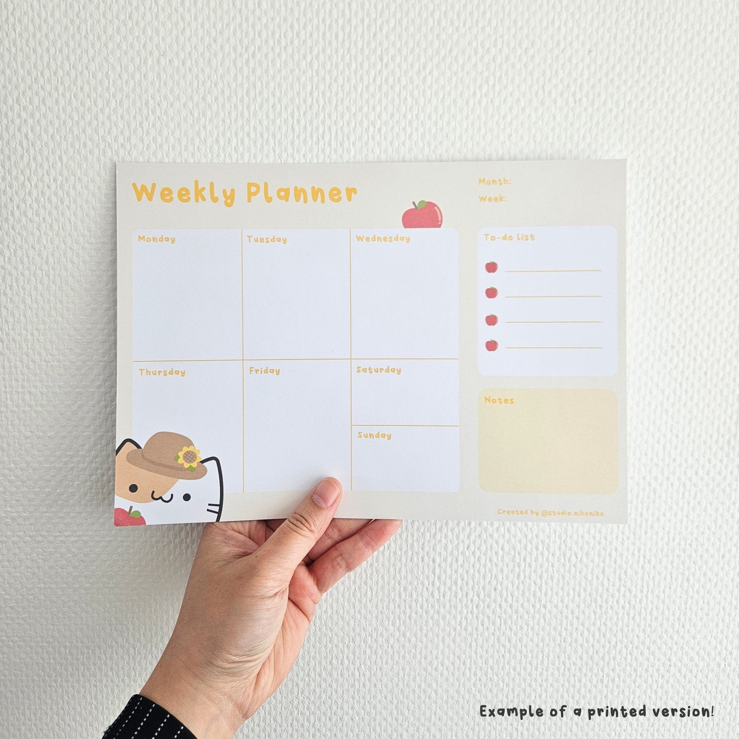 A hand holding a printed version of the yellow weekly planner with apples