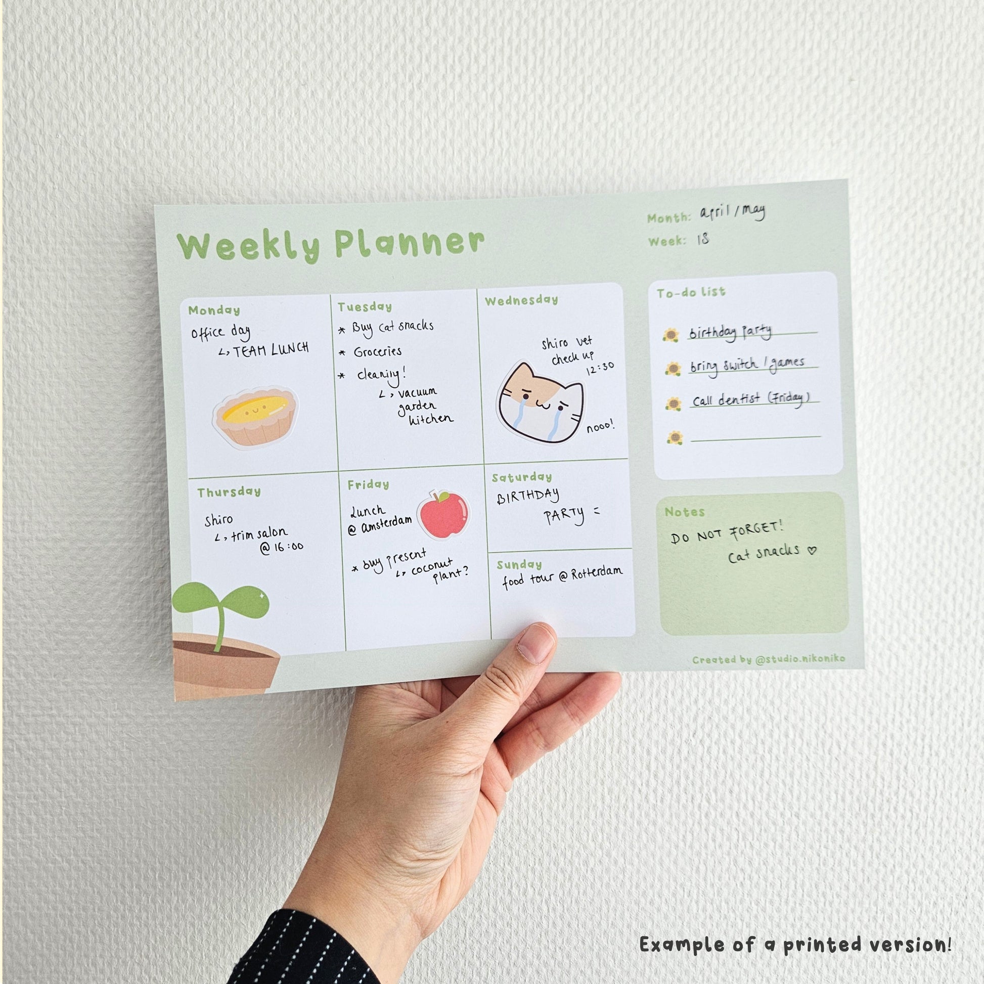 A hand holding a green weekly planner that is decorated with stickers and text